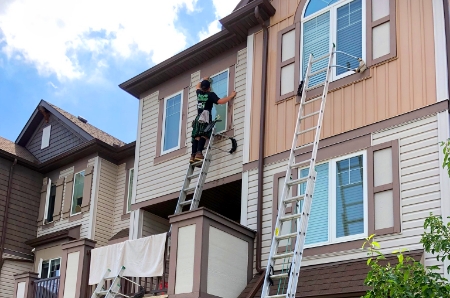 A Men In Kilts technician standing on a ladder to clean upper-story windows.