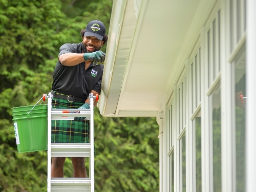 A courteous Men in Kilts team member cleaning residential gutters 