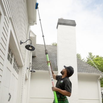 A Men in Kilts technician using a low-pressure cleaning tool to clean exterior.