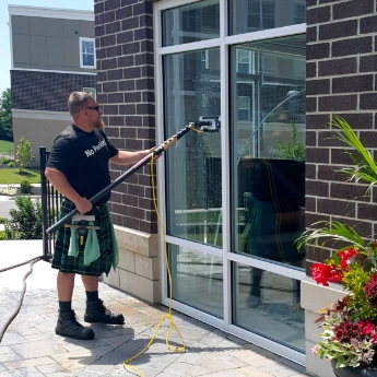 A Men In Kilts Technician cleaning the windows of a business.
