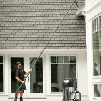 A Men In Kilts technician cleaning second-story gutters with a gutter vacuum.