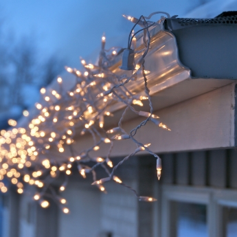 Lit residential holiday lights hanging from a gutter at night. 