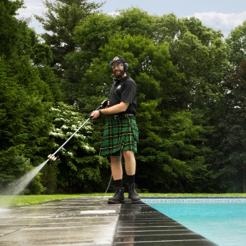  A Men In Kilts technician using a professional grade pressure washer next to a pool. 