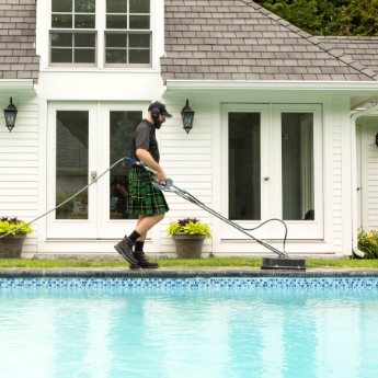 A Men In Kilts technician using a professional-grade pressure washer next to a pool
